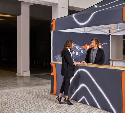 Printed Ecotent® folding gazebo with counter and two people in conversation.