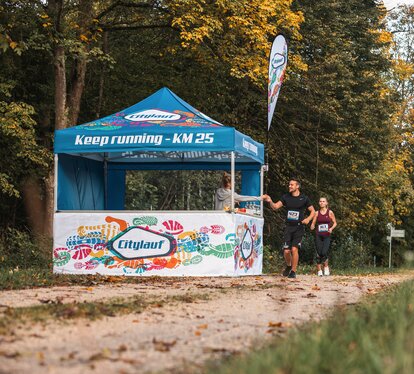Blue 3x3m event gazebo with custom Citylauf print, with custom flag, closed side wall and half-height side wall with counter used as a refreshment stand at a city race